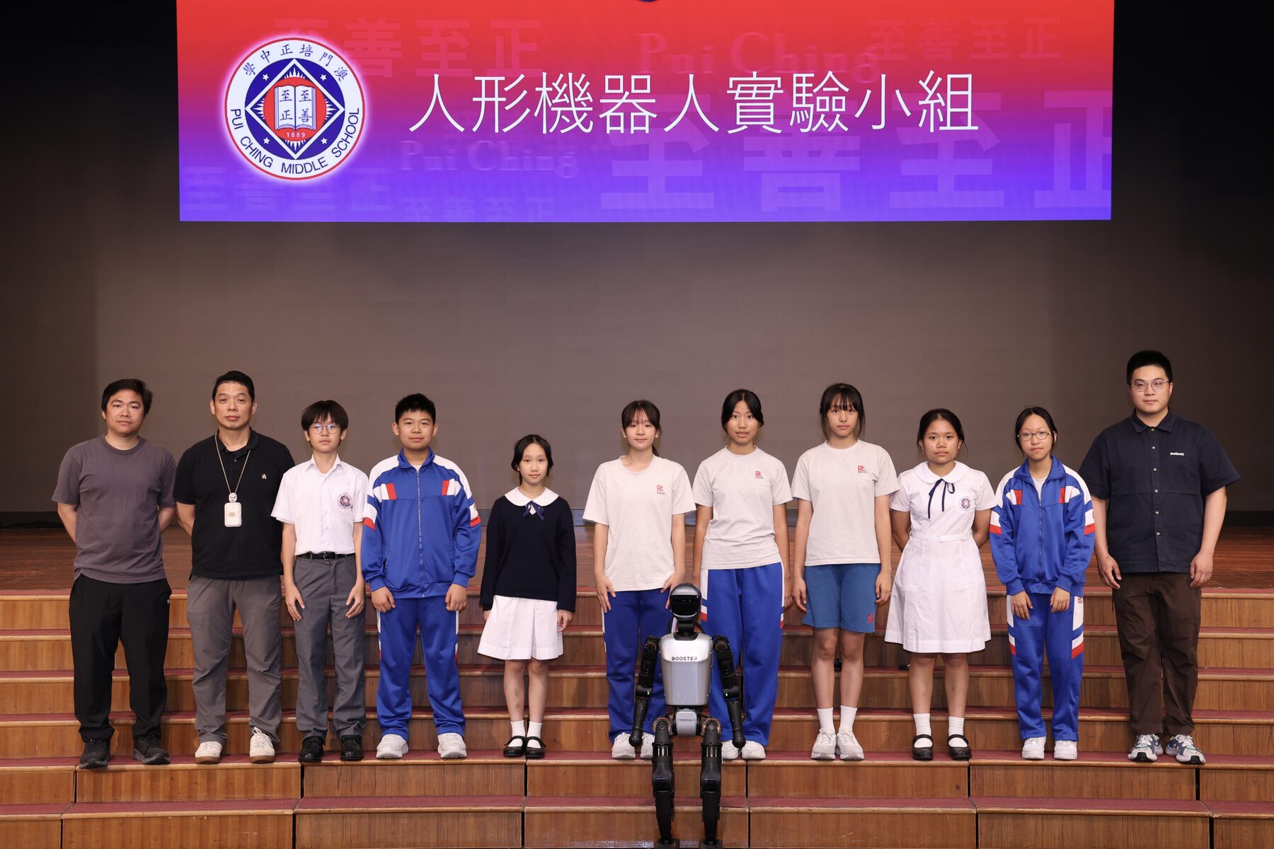 The 2025–26 PCMS-HRG students and coaches on stage with a Booster T1 robot