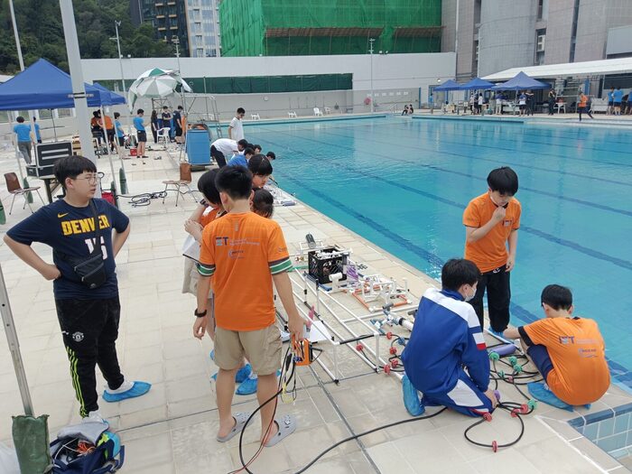 Students rigging their vehicles on an outdoor pool deck beside competition tents