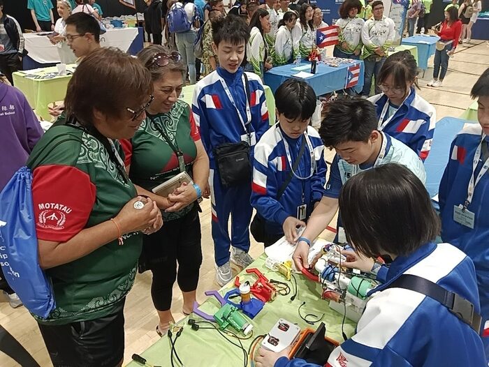 Pui Ching students showing their vehicle and printed parts to visitors from another team at an indoor venue