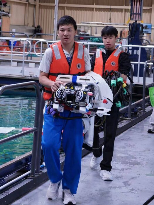 Two students in life jackets carrying the ROV along a dock
